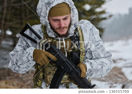 Soldier In Winter Camouflage Adjusting Rifle During Snowy Military Training Exercise In Forest 136555709