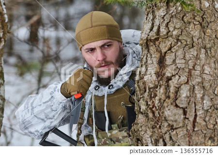 Soldier in Winter Camouflage Hiding Behind Tree With Tactical Knife and Radio 136555716