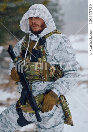 Armed Soldier in Winter Camouflage With Tactical Vest and Rifle Standing in Snowy Forest 136555729