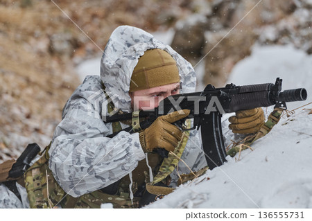 Soldier in Winter Camouflage Aiming Rifle While Lying in Snow During Military Training Exercise 136555731