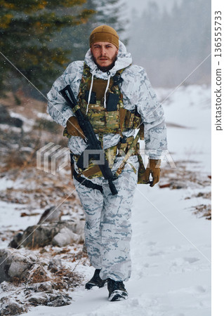 Soldier In Winter Camouflage Walking Through Snowy Forest With Rifle And Tactical Gear 136555733