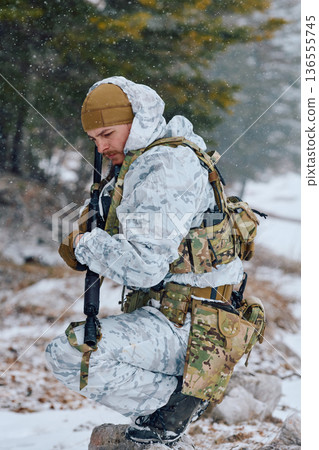 Soldier In Winter Camouflage Gear Kneeling With Rifle During Snowy Military Training Exercise 136555745