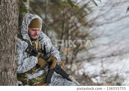 Soldier In Winter Camouflage Resting Against Tree With Rifle During Cold Training Patrol 136555755