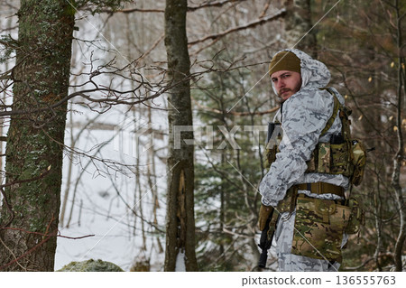Soldier In White Winter Camouflage Patrols Snowy Forest While Looking Back Over Shoulder 136555763