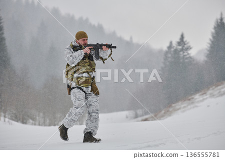 Armed Soldier in Winter Camouflage Patrols Snowy Forest With Rifle and Tactical Gear 136555781