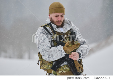 Soldier In Winter Camouflage Adjusting Gloves During Snowy Training With Tactical Gear And Rifle 136555805