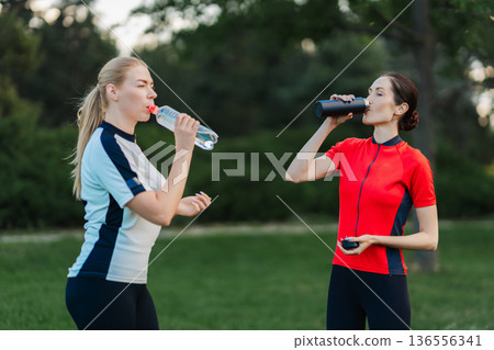 Women drink water during outdoor workout session Women drink water during outdoor workout session 136556341