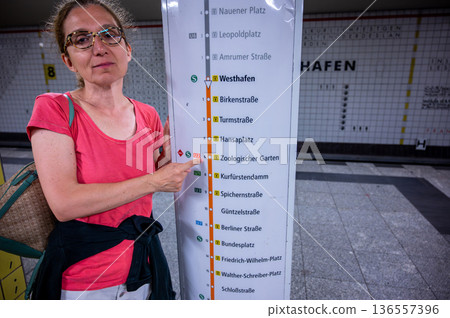 Berlin, germany, august 14, 2023. Woman at berlin u-bahn station pointing to zoologischer garten stop on subway map, navigating urban public transport journey 136557396