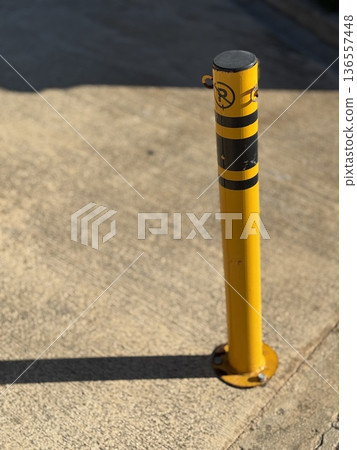 Yellow parking bollard casting shadow on pavement in bright sunlight, ideal for background use Yellow parking bollard casting shadow on pavement in bright sunlight, ideal for background use 136557448