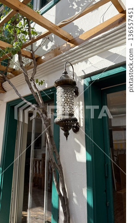 Exterior wall light with decorative design on white facade surrounded by greenery and wood trellis 136557451
