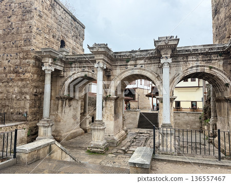 Ancient Roman triumphal arch with three arches and historical stone architecture in overcast weather Ancient Roman triumphal arch with three arches and historical stone architecture in overcast weather 136557467