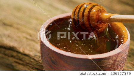 Honey dripping from a wooden stick into a bowl on a wooden surface at a local market in the afternoon 136557579