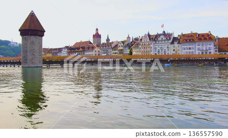 Historic buildings line the shore of Lake Lucerne with wooden bridge and tower in the foreground on a sunny day in Switzerland Historic buildings line the shore of Lake Lucerne with wooden bridge and tower in the foreground on a sunny day in Switzerland 136557590