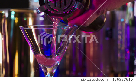 Bartender pours liquid into a martini glass at a bar during nightlife hours Bartender pours liquid into a martini glass at a bar during nightlife hours 136557610