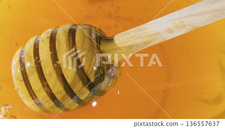 Honey drips from a wooden dipper into a bright orange bowl at a kitchen counter during daytime Honey drips from a wooden dipper into a bright orange bowl at a kitchen counter during daytime 136557637