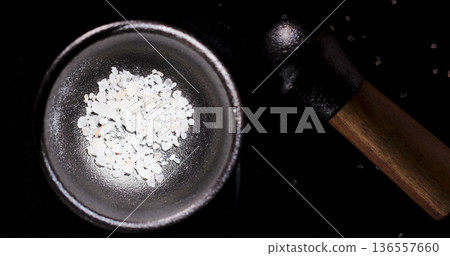 Crushed salt in a bowl with a pestle on a dark surface during evening cooking preparation 136557660