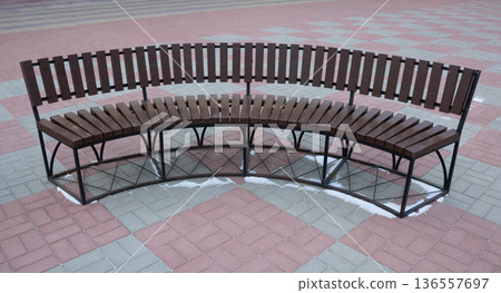 A brown semi-circular bench in a park square. 136557697
