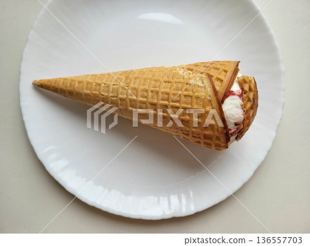Broken brown ice cream cone on a white plate. Broken brown ice cream cone on a white plate. 136557703