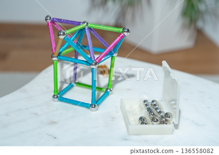 Magnetic building structure made of bright rods and steel spheres on a white table. Indoor lifestyle scene. Concept of early education, imagination, engineering thinking and child development. Magnetic building structure made of bright rods and steel spheres on a white table. Indoor lifestyle scene. Concept of early education, imagination, engineering thinking and child development. 136558082