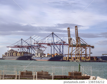 Cargo Ships and Container Cranes at Busy Commercial Port Under Cloudy Sky Cargo Ships and Container Cranes at Busy Commercial Port Under Cloudy Sky 136558212