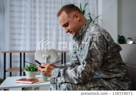 Soldier in camouflage uniform using smartphone at home 136559071