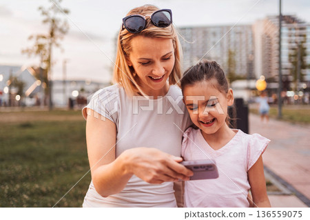 Mother and daughter looking at smartphone and smiling in the park 136559075