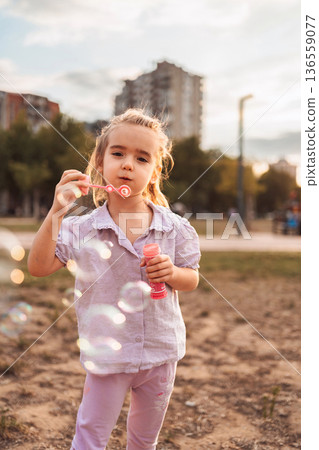 Little girl blowing soap bubbles in the park Little girl blowing soap bubbles in the park 136559077