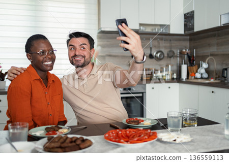 Happy multi-ethnic couple taking a selfie while having lunch in the kitchen Happy multi-ethnic couple taking a selfie while having lunch in the kitchen 136559113