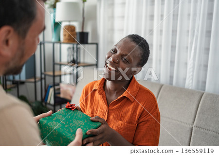 Man giving a gift to a surprised woman at home 136559119