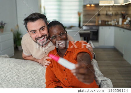 Excited multi-ethnic couple sharing pregnancy test results at home 136559124