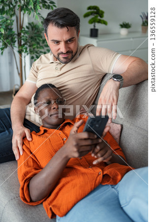 Interracial couple relaxing on sofa using smartphone at home 136559128