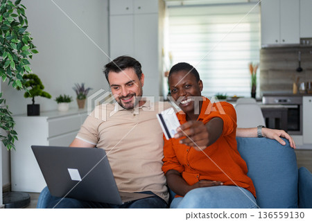Happy couple buying online with credit card and laptop at home Happy couple buying online with credit card and laptop at home 136559130
