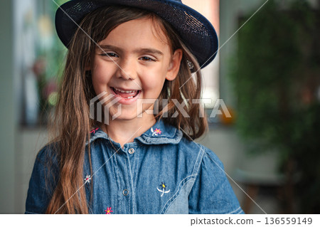Portrait of smiling preschool age girl wearing a hat and a denim dress 136559149