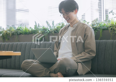 一個男人坐在沙發上使用電腦 136559351