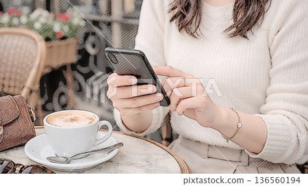 一位女士在咖啡館的露台座位上使用智慧型手機 136560194