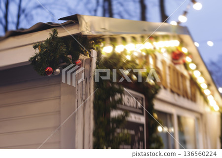 Christmas market with illuminated food stalls, gift shops and kiosks, New Year outdoor fair decorations, garlands and festoons, Xmas atmosphere, retail and store illumination, decor in Europe city Christmas market with illuminated food stalls, gift shops and kiosks, New Year outdoor fair decorations, garlands and festoons, Xmas atmosphere, retail and store illumination, decor in Europe city 136560224