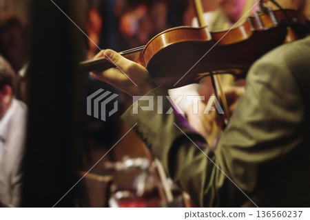 Concert view of violinist with vocalist and musical band, fiddler performing classical music, symphony orchestra performing music, violin player on stage in a club, music arena hall, fiddle and bow 136560237