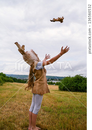 Girl in bunny costume and hat with long ears, playing with stuffed toy in field under cloudy sky 136560532