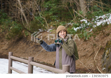 Woman holding binoculars and pointing outdoors in winter 136563975