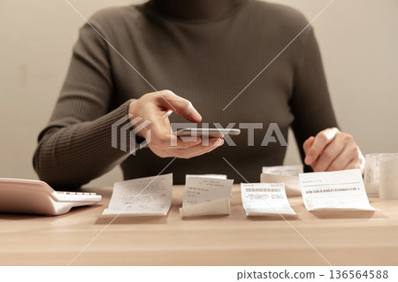Women using smartphone calculate paper receipts on table. Calculating bills, expense tracking, personal finance Women using smartphone calculate paper receipts on table. Calculating bills, expense tracking, personal finance 136564588