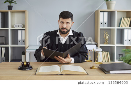 Judge signing case documents at desk with gavel, open law book and scales Judge signing case documents at desk with gavel, open law book and scales 136564903