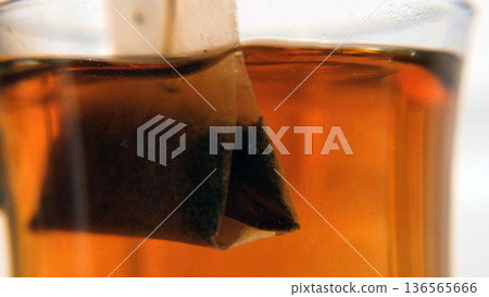 Teabag steeping in hot water, color diffusing slowly. Macro view of the tea brewing process, morning calm and breakfast concept Teabag steeping in hot water, color diffusing slowly. Macro view of the tea brewing process, morning calm and breakfast concept 136565666