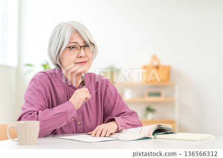 一位老年婦女一邊學習一邊查看教材。 一位老年婦女一邊學習一邊查看教材。 136566312