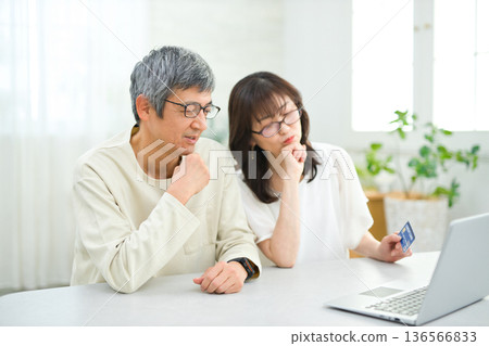 A couple in their 60s looking at a computer and cards in the living room A couple in their 60s looking at a computer and cards in the living room 136566833