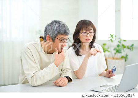 一對六十多歲的夫婦在客廳看著電腦和撲克牌。 136566834