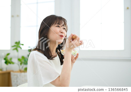 A woman in her 60s eating salad in the living room 136566845