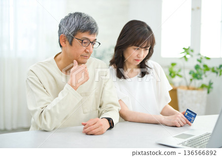 A couple in their 60s looking at a computer and cards in the living room A couple in their 60s looking at a computer and cards in the living room 136566892