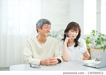 A couple in their 60s looking at a computer and cards in the living room 136566912