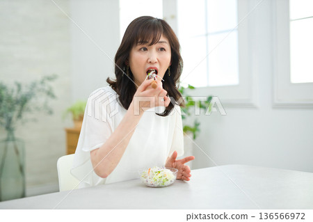 A woman in her 60s eating salad in the living room A woman in her 60s eating salad in the living room 136566972