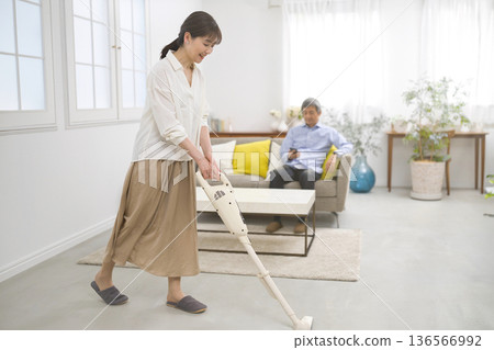 一位微笑的女士和一位六十多歲的男士一邊用吸塵器打掃一邊交談。 一位微笑的女士和一位六十多歲的男士一邊用吸塵器打掃一邊交談。 136566992